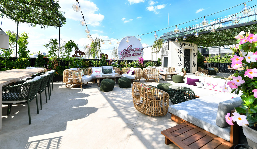 Summer day at Grace Garden terrace in Berlin. Dining setup with dining chairs and tree table, Cane-line Nest lounge furniture nature, blooming flowers 