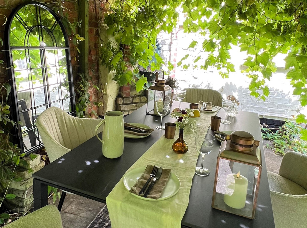 Pergola with grapevines from ceiling, white bouclé outdoor chairs, outdoor garden table, white table runner, glas, dishes, cosy setting