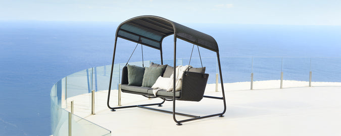 Modern swing seat with grey cushions and black frame overlooking a scenic view.