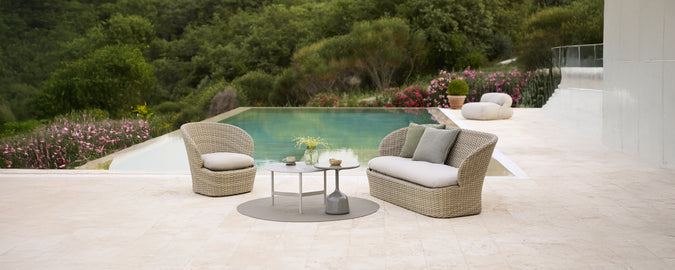 Modern grey sofa with cushions and round table by a poolside.