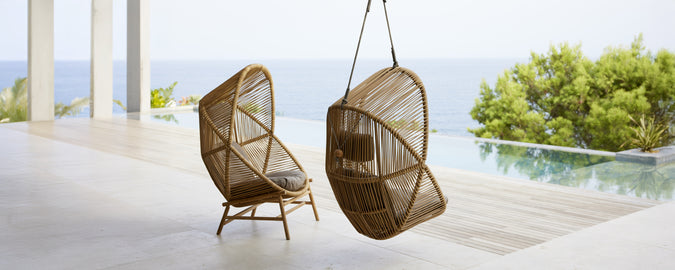 Two modern hanging chairs in a contemporary setting overlooking water.