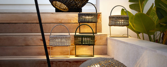 A collection of black, grey, and green lanterns on wooden stairs with greenery.