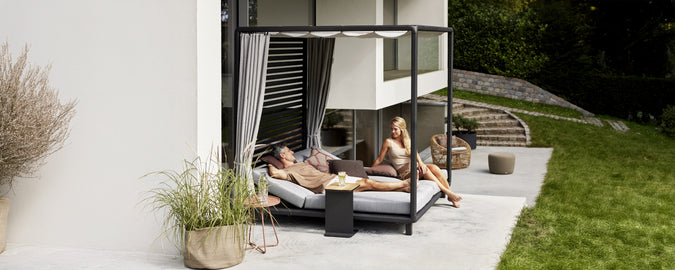 Modern outdoor lounge area featuring a black daybed with grey cushions and white curtains.