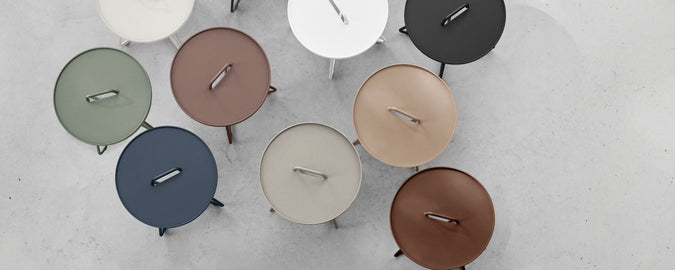 Collection of modern round tables in various colors arranged on a light surface.