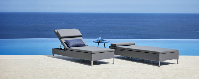 Grey lounge chair and chaise lounge beside a pool with a view of the ocean.