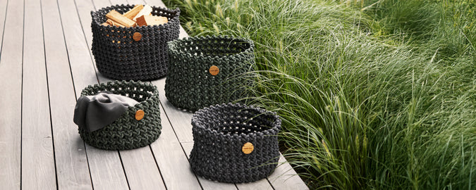 Collection of black woven baskets arranged on a wooden deck with greenery in the background.