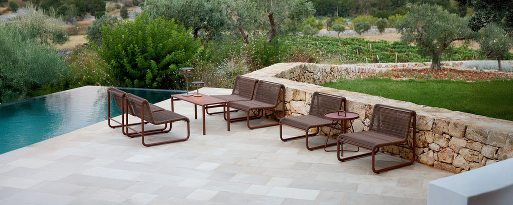Modern brown lounge chairs and table by a poolside in an outdoor setting.
