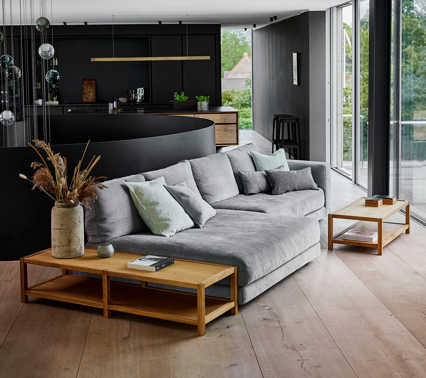 Modern living space featuring a gray sectional sofa adorned with pillows, complemented by wooden side tables and decorative plant arrangements.