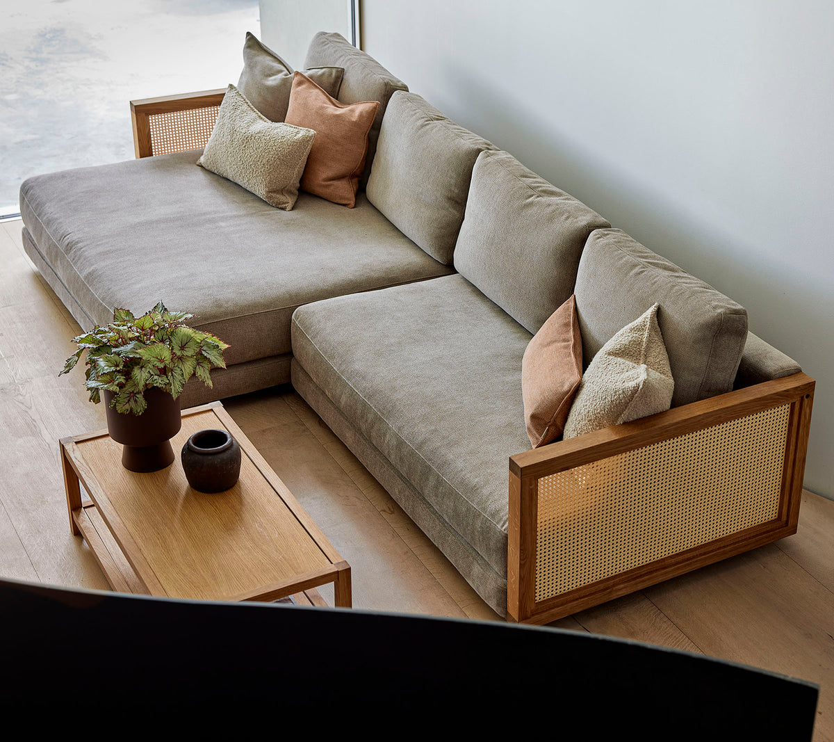 A stylish sectional sofa with soft cushions and decorative pillows, paired with a wooden coffee table featuring plants and elegant decor.