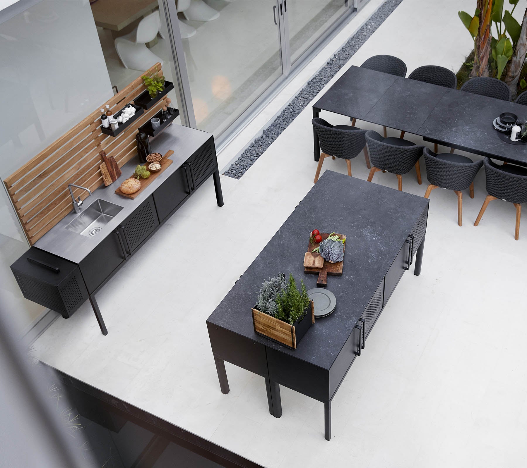 Modern outdoor kitchen setup featuring a sleek countertop, spacious dining table, and stylish seating arrangement with plants and decor elements.