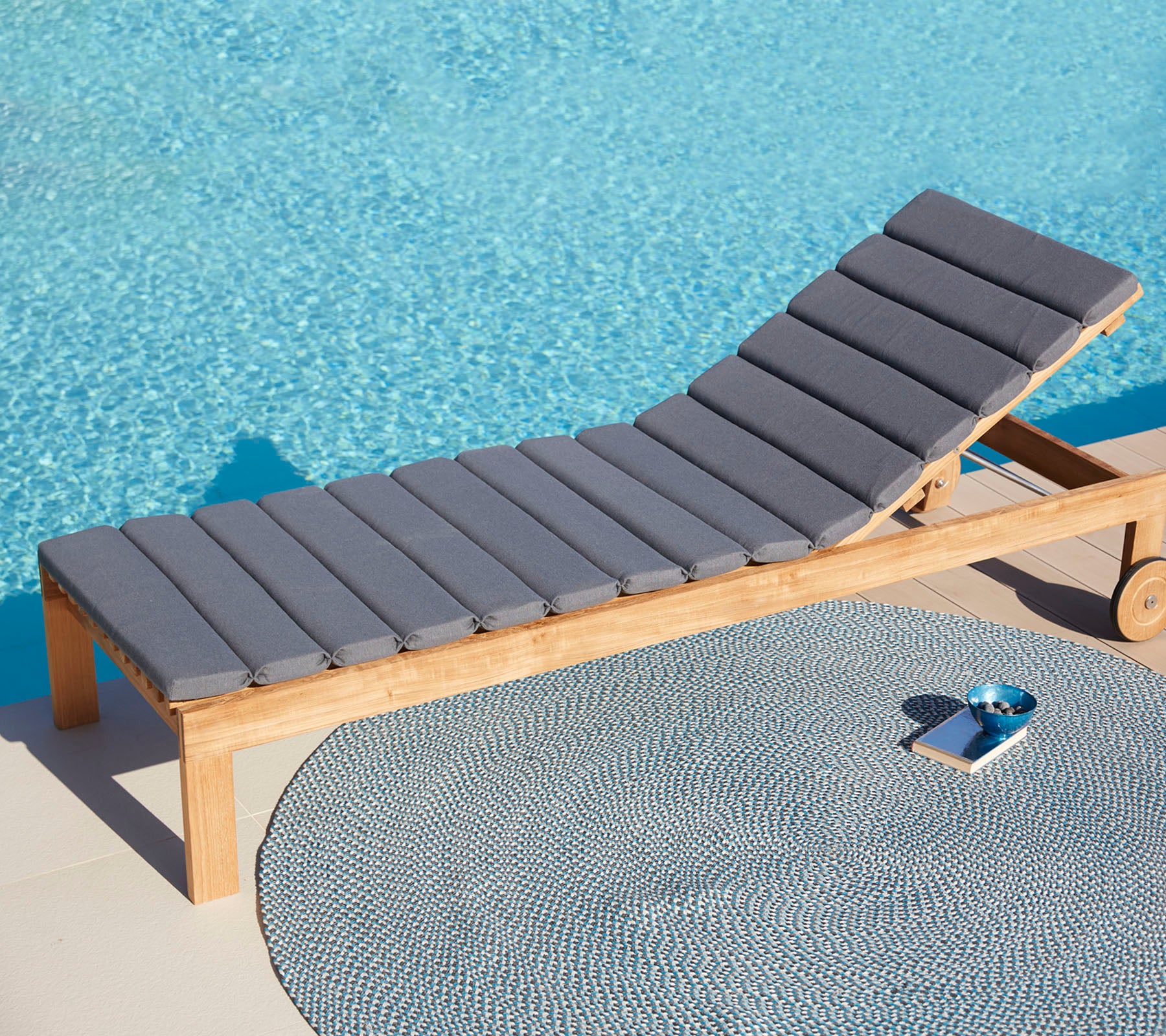 Comfortable gray lounge chair beside a circular mat and a small tray, with a tranquil blue water surface in the background.