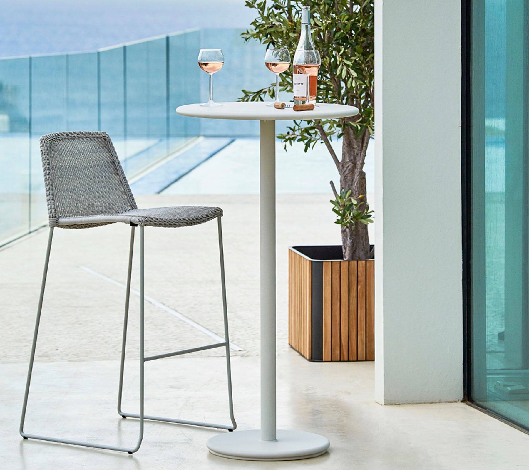 Stylish outdoor setting with a high table, a gray bar stool, and two glasses of rosé paired with a bottle on the table.