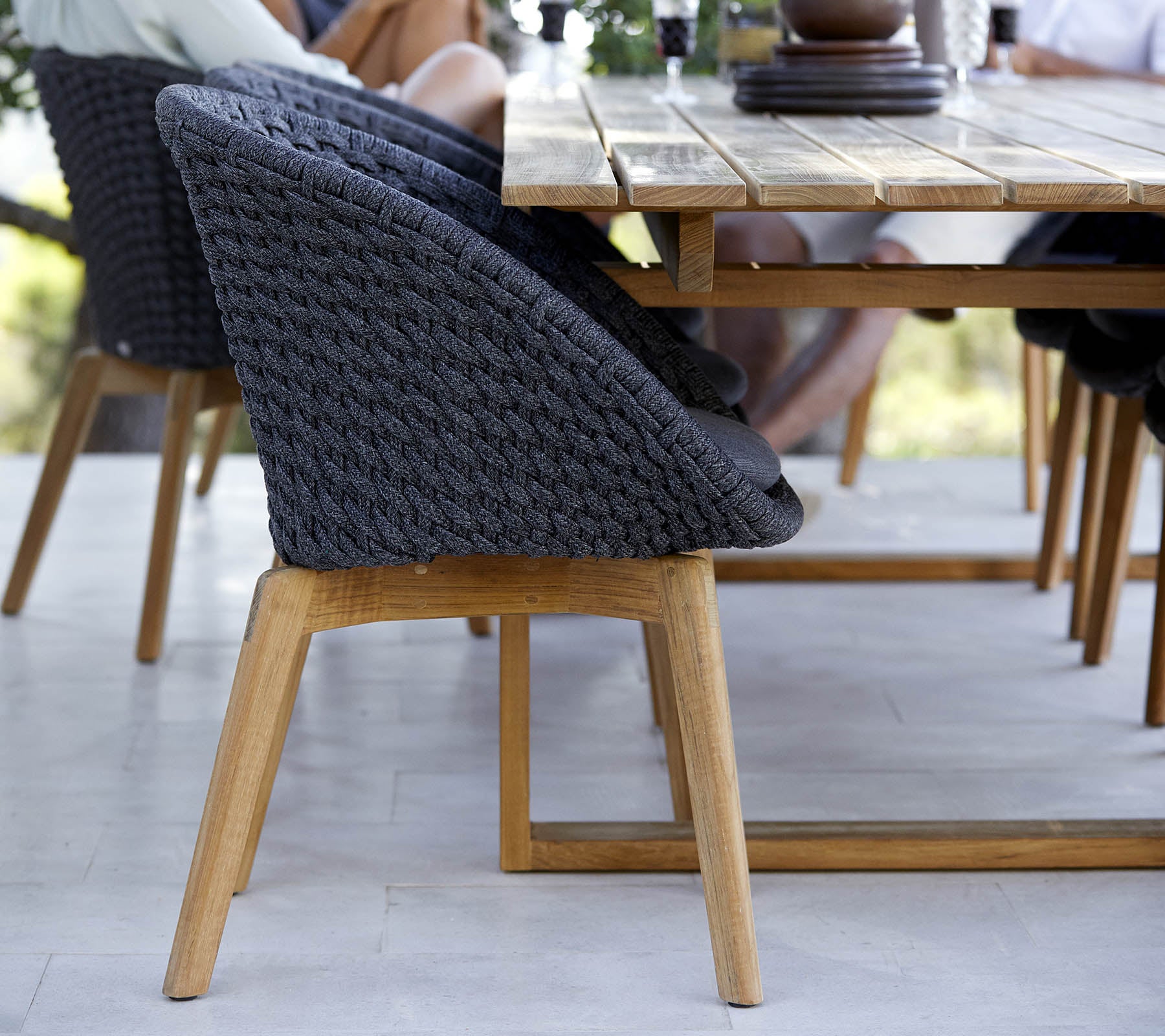 Stylish woven chair with a wooden base, positioned beside a table, showcasing a modern design perfect for gathering spaces.