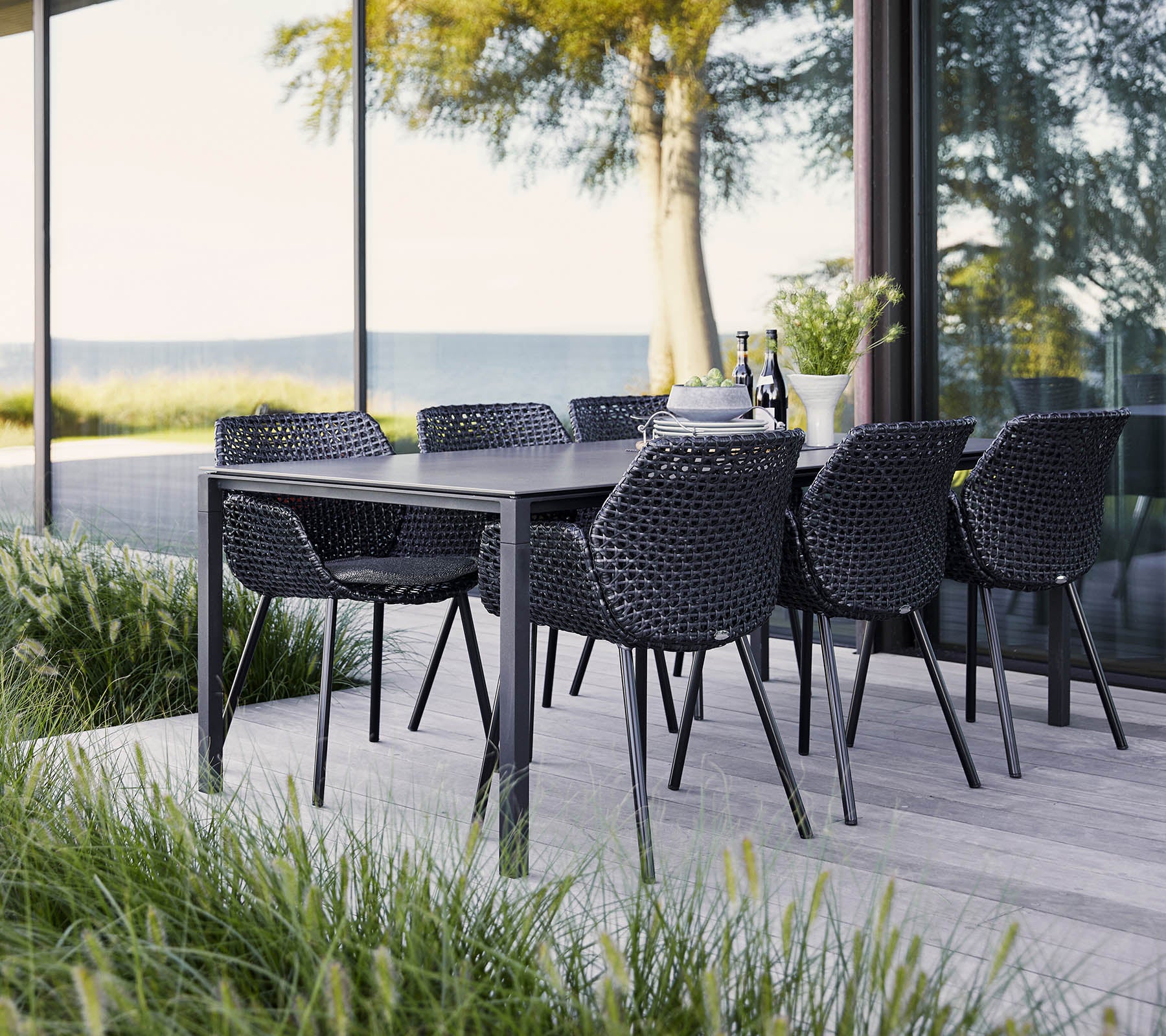 A stylish dining set with a black table and woven chairs, surrounded by lush greenery and expansive views. Ideal for gatherings.