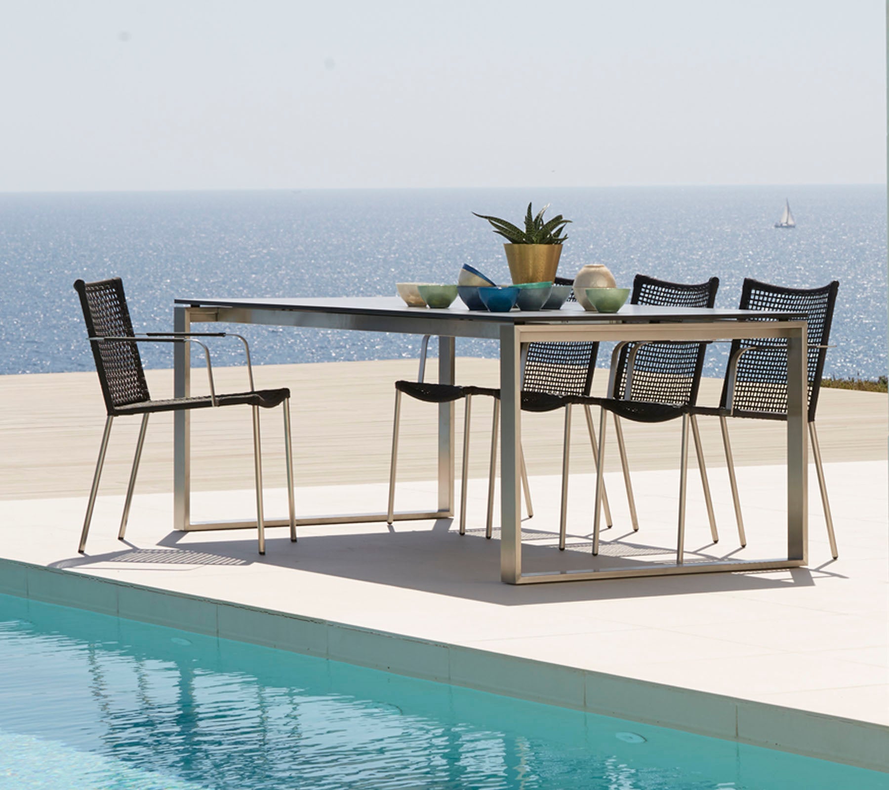 A modern dining table surrounded by sleek chairs, adorned with decorative items, overlooking a tranquil sea view.