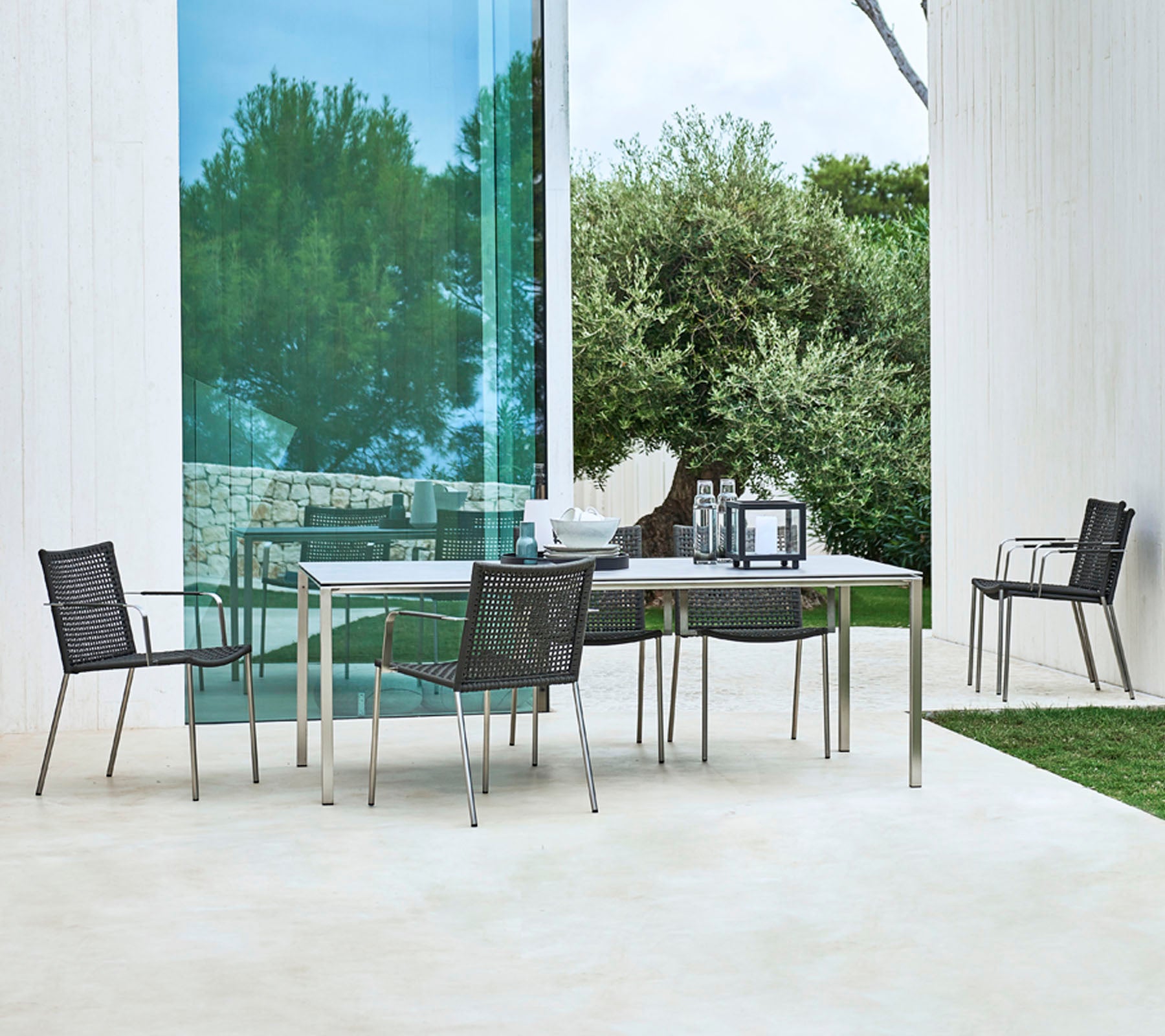 A modern outdoor dining set featuring a rectangular table and four stylish chairs with a sleek design, surrounded by greenery.