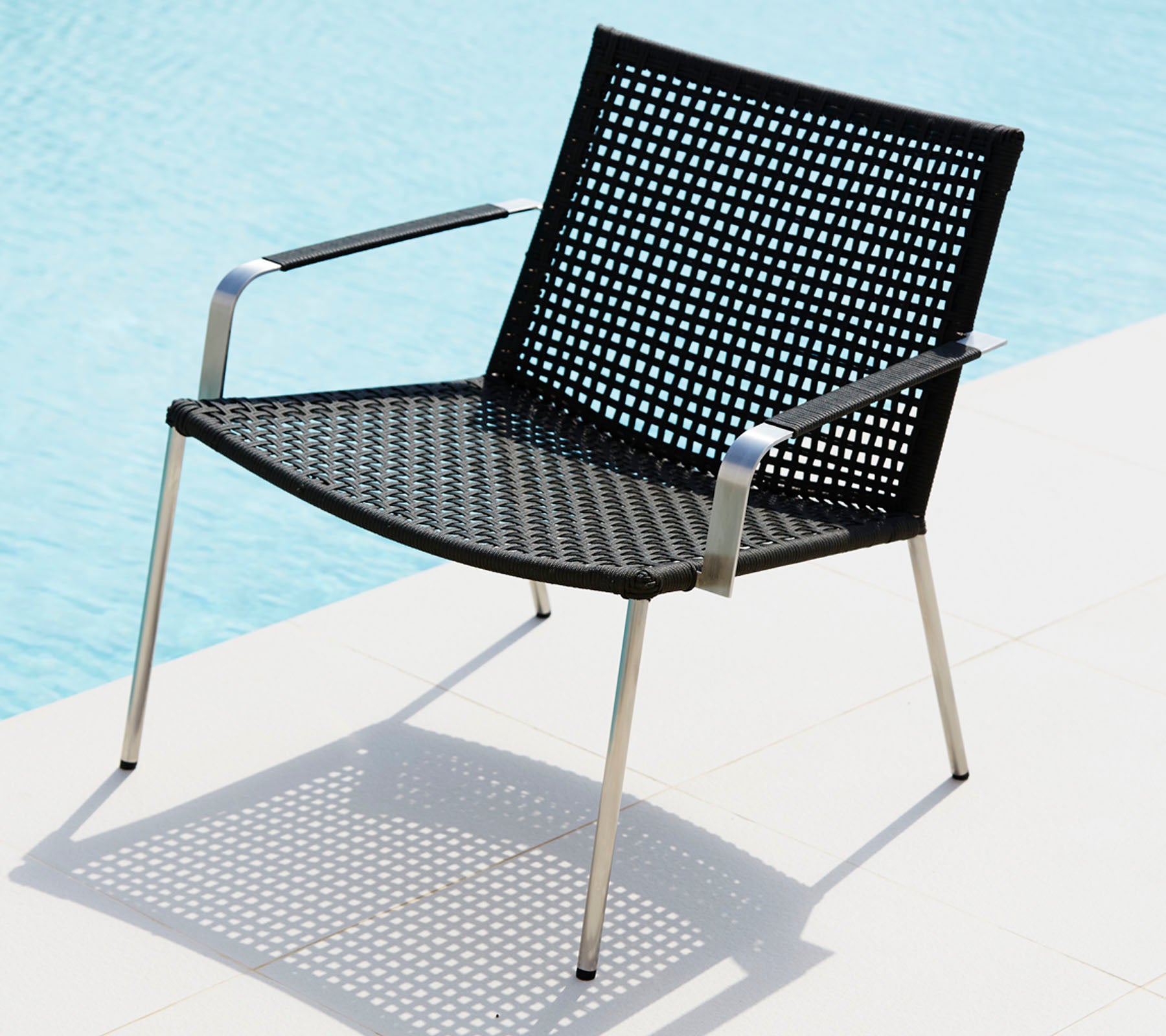 Stylish black chair with a perforated design and sleek metal legs, casting a shadow on a light surface.