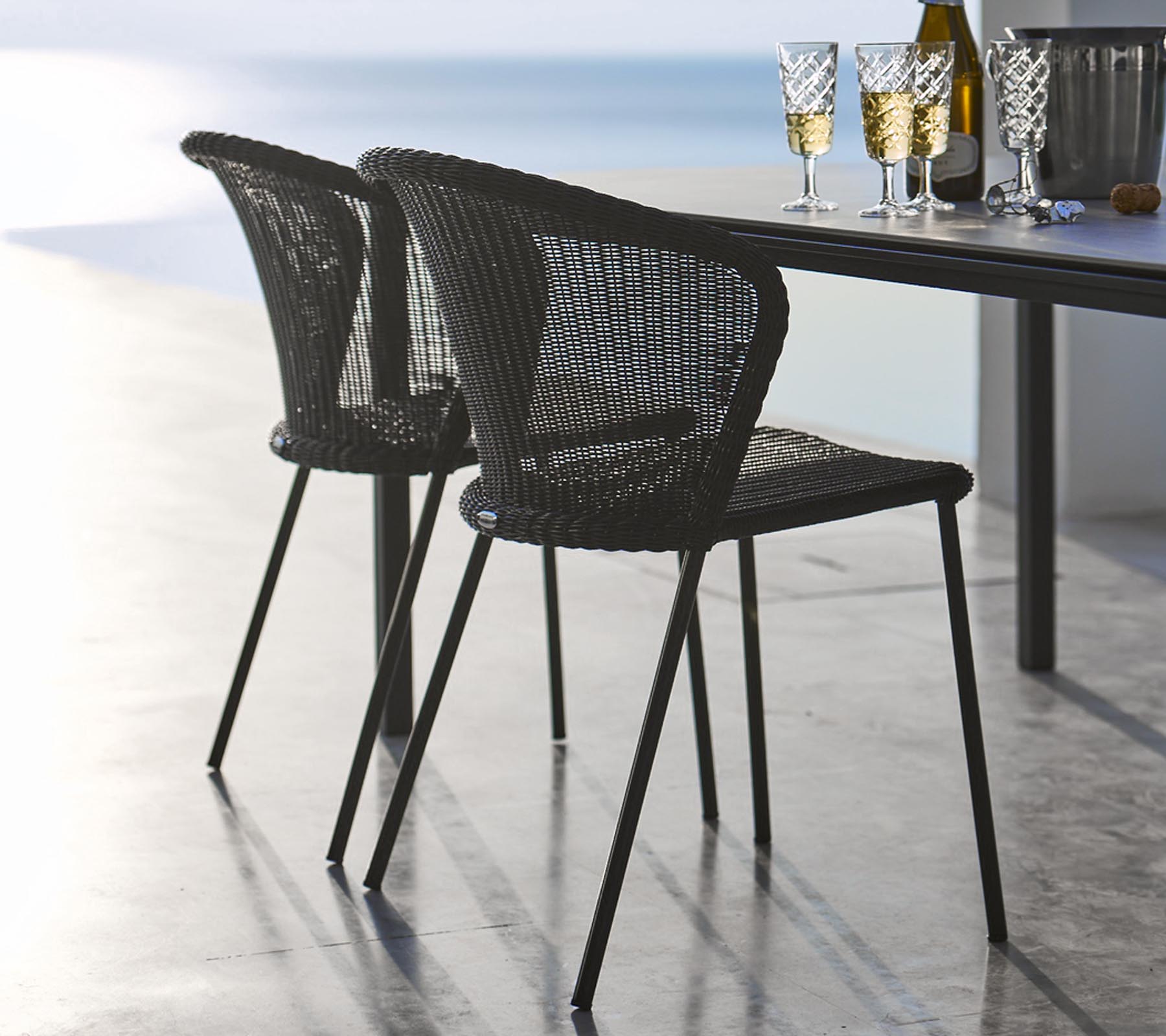 Two stylish black woven chairs positioned beside a table set with glasses and a bottle, evoking a relaxed dining atmosphere.