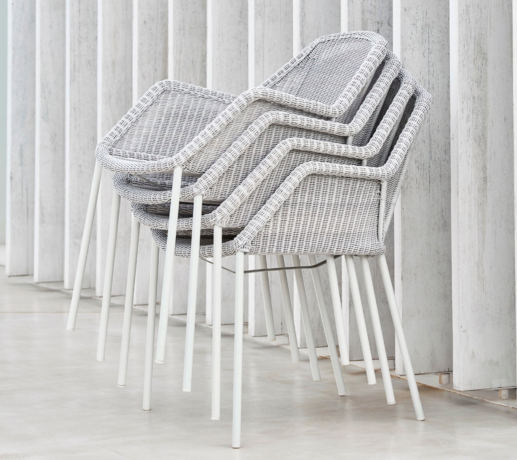 Stacked modern chairs with a woven design in grey and white, resting against vertical surfaces, showcasing a sleek and minimalist aesthetic.