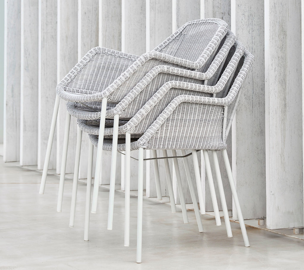 Stacked modern chairs with a woven design in grey and white, resting against vertical surfaces, showcasing a sleek and minimalist aesthetic.