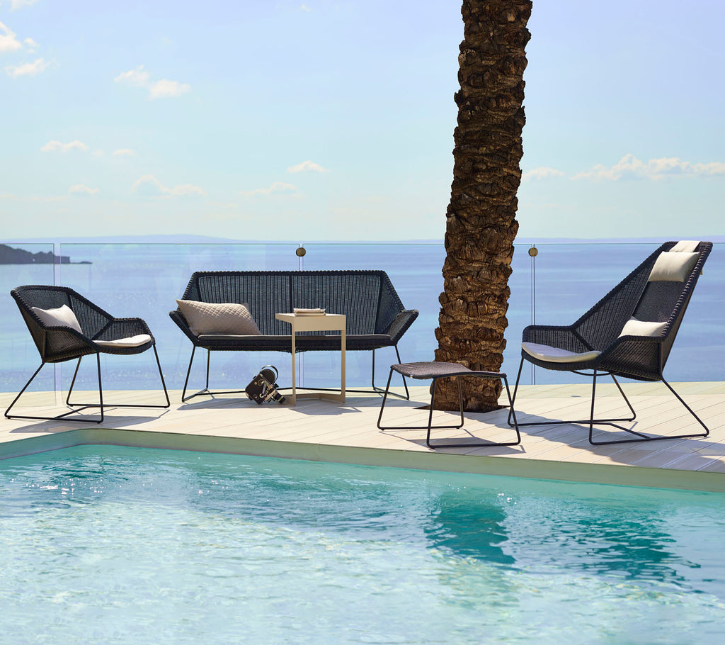 Modern lounge seating with black chairs and loveseat beside a pool.
