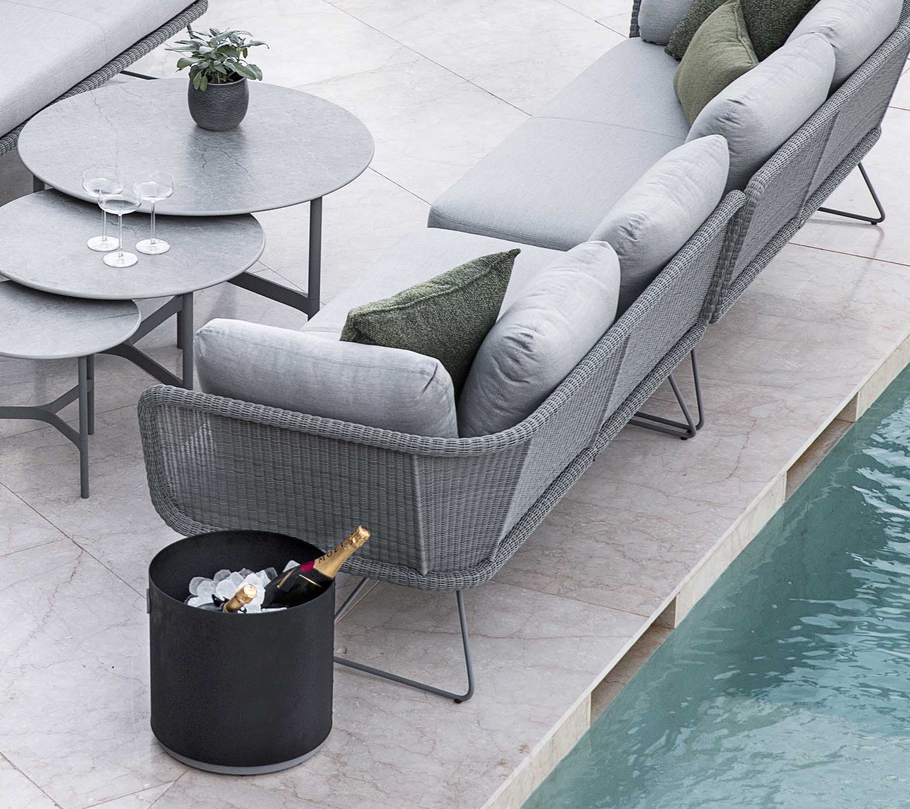 Modern outdoor seating arrangement featuring a stylish gray sofa and a round table, complemented by a bucket of ice and drinks.