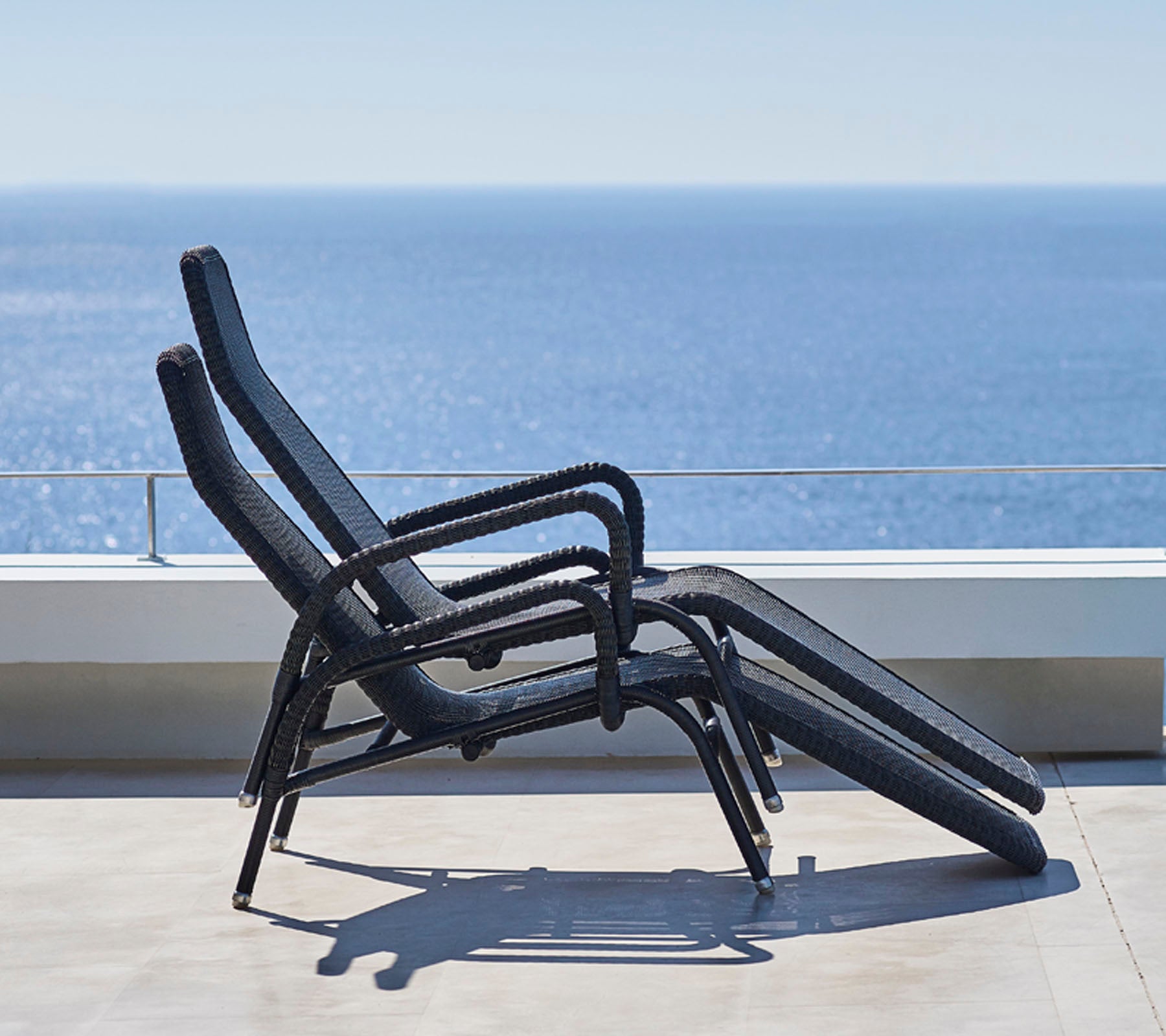 Three reclining lounge chairs are stacked against a backdrop of a serene ocean view, showcasing a minimalist outdoor relaxation space.
