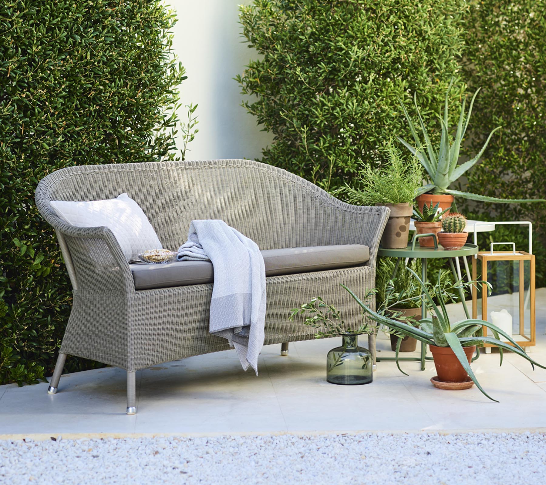 A cozy loveseat with decorative pillows, accompanied by potted plants and a side table, surrounded by greenery.