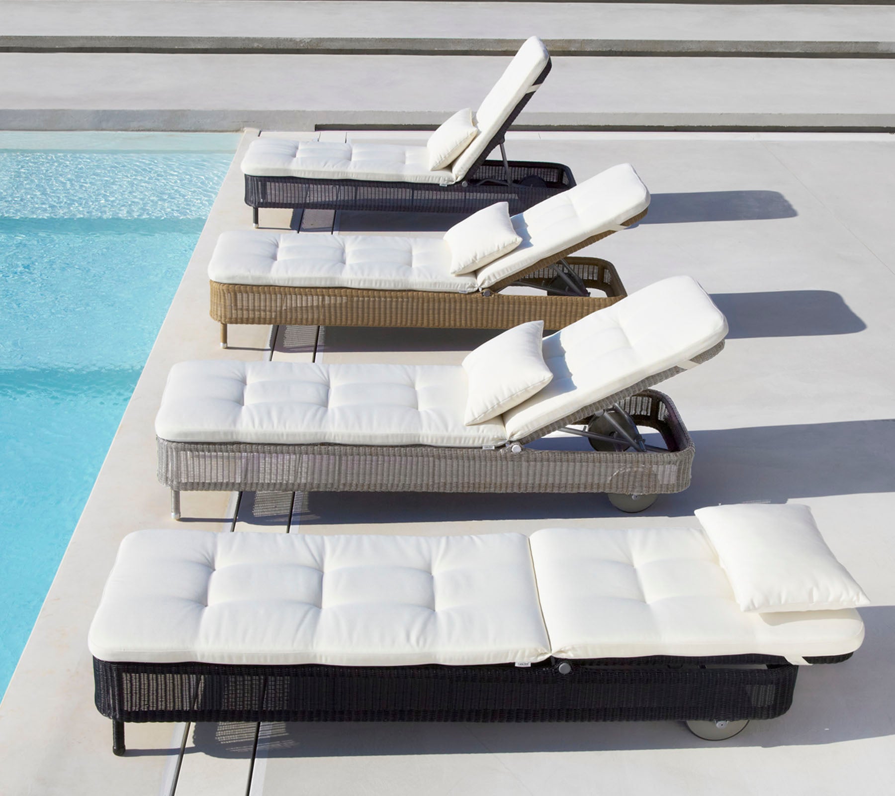 Four loungers in various colors with white cushions, positioned beside a pool, each with an adjustable backrest.