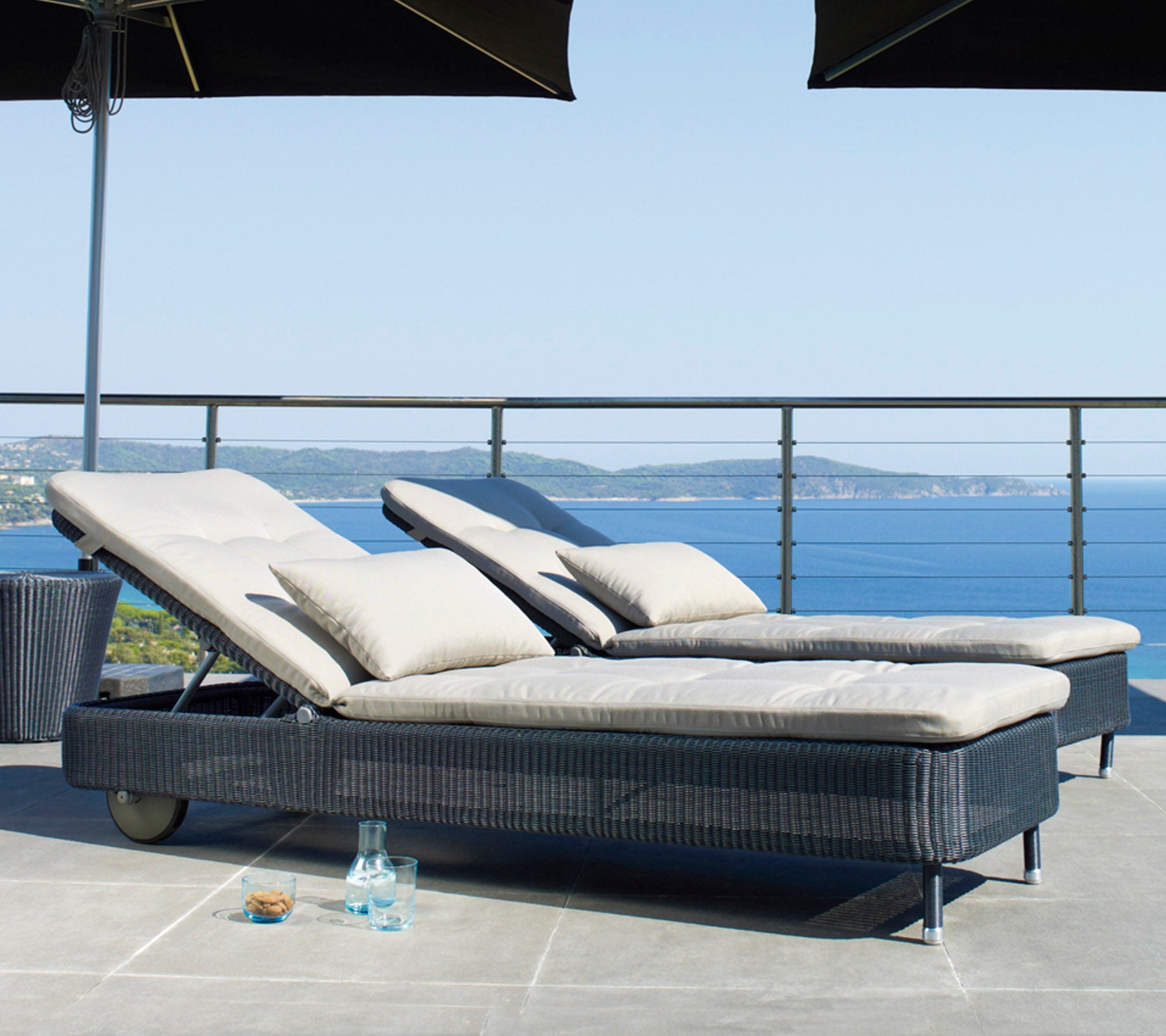 Two reclining lounge chairs with plush cushions, placed near a railing, with a serene ocean view in the background.