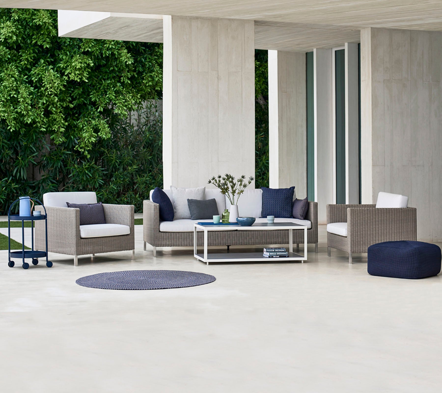 Contemporary outdoor seating area featuring a sofa, armchairs, and a coffee table, complemented by decorative cushions and a round rug.