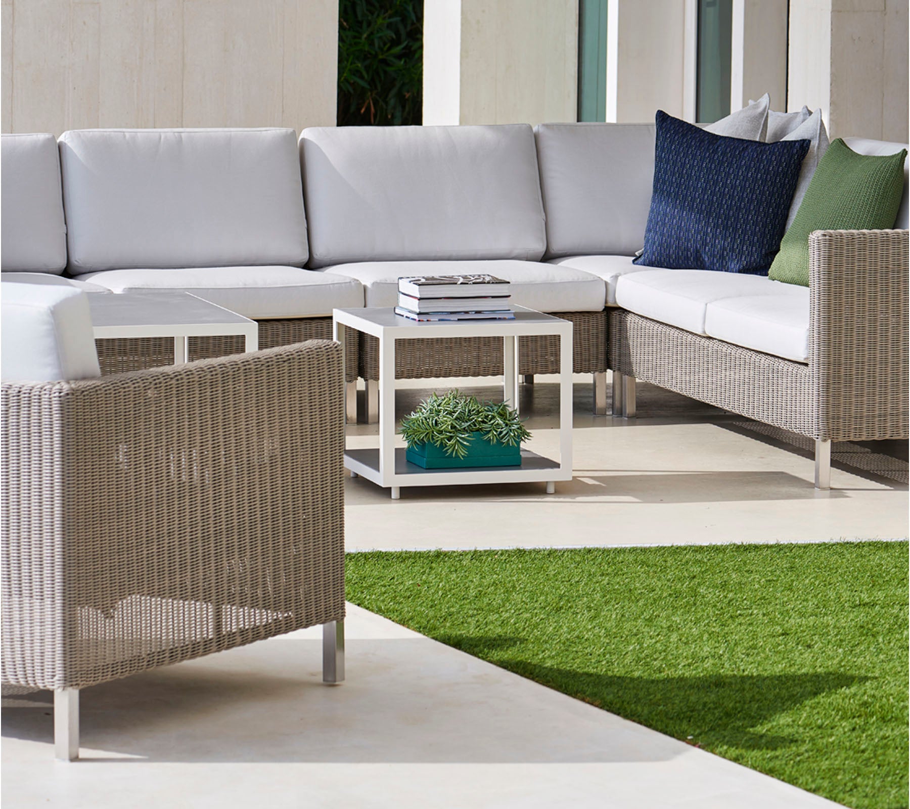 Stylish outdoor seating area featuring a sectional sofa with gray cushions, cozy pillows, and a modern coffee table on a lush green surface.