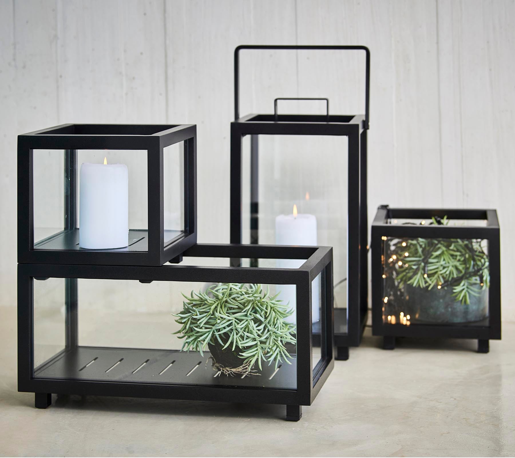 A set of elegant candle holders featuring black frames and glass panels, displaying plants and candles in various sizes.