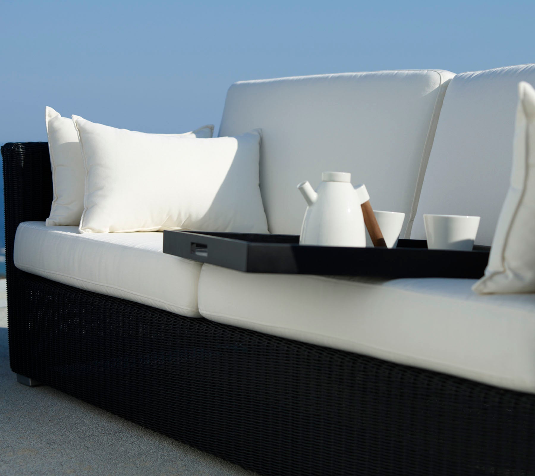 Stylish sofa with white cushions and a black frame, featuring a tray with a teapot and cups for a cozy setting.
