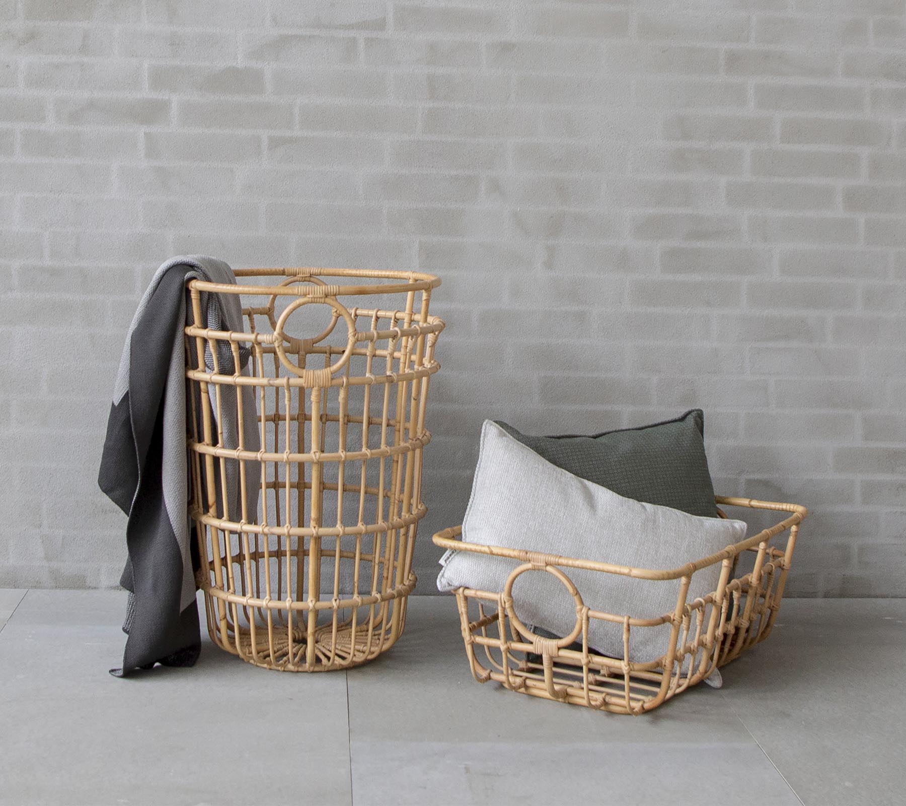 Two wicker baskets in natural tones; one tall with a throw draped over it, and a smaller one filled with cushioned pillows.