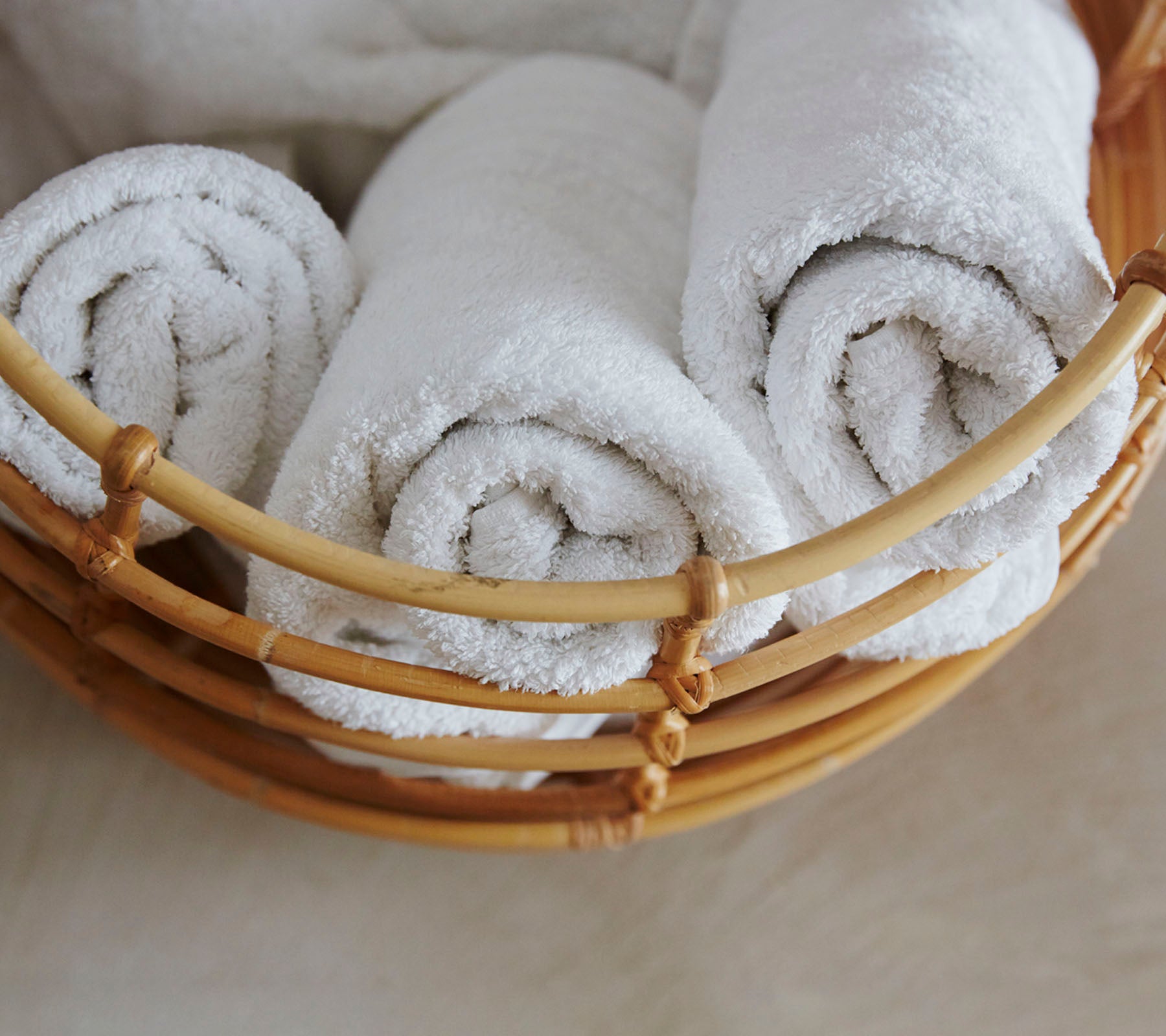 A woven basket filled with neatly rolled, fluffy white towels.