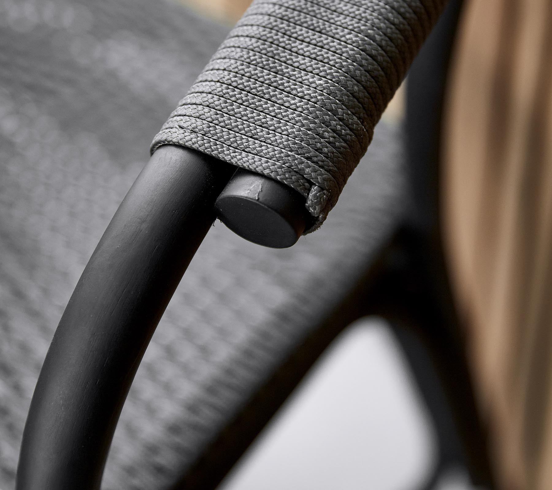 Close-up of a stylish chair's armrest featuring a sleek black frame and textured gray wrapping for comfortable grip.