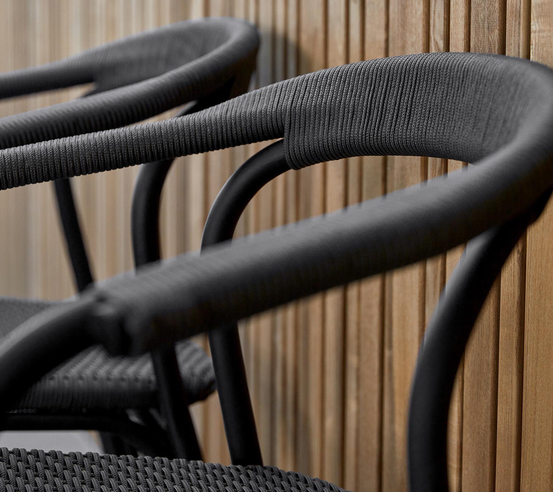 Three stylish black chairs featuring curved arms, designed with a textured finish, against a warm wooden backdrop.