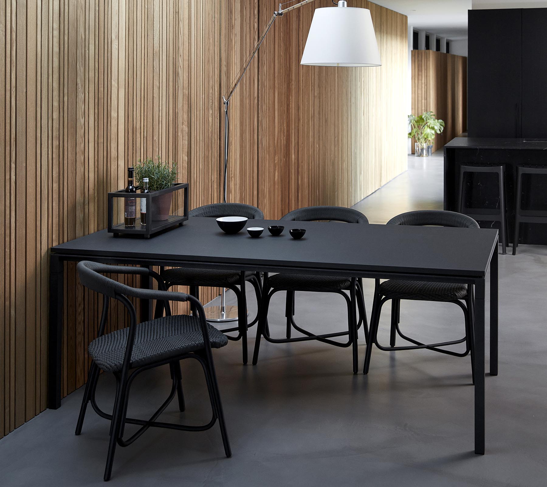 A sleek black dining table accompanied by chairs, set with bowls and decorative items, against a backdrop of wooden panels.