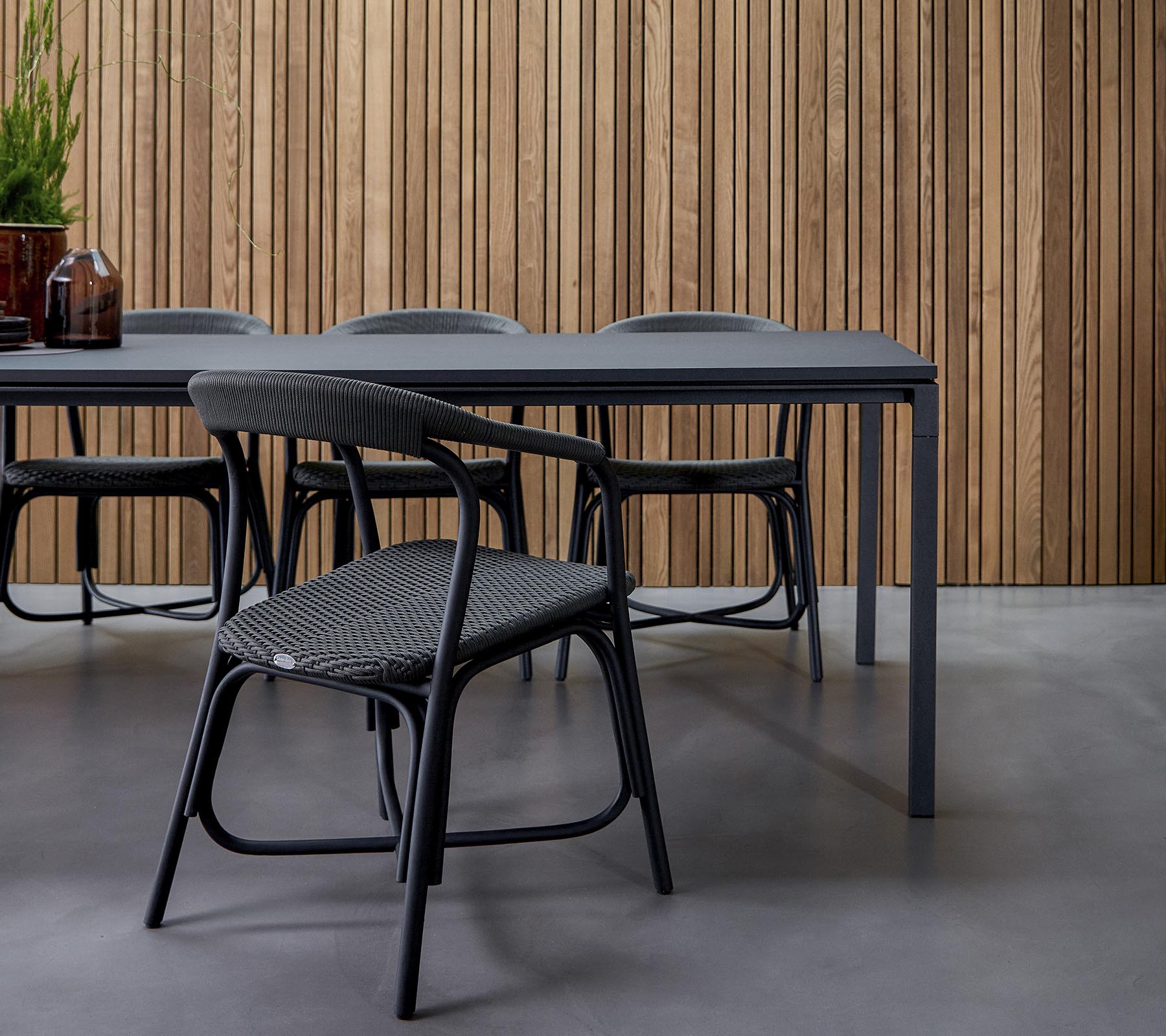 A modern dining area featuring a sleek table surrounded by stylish chairs, set against a textured wooden backdrop.