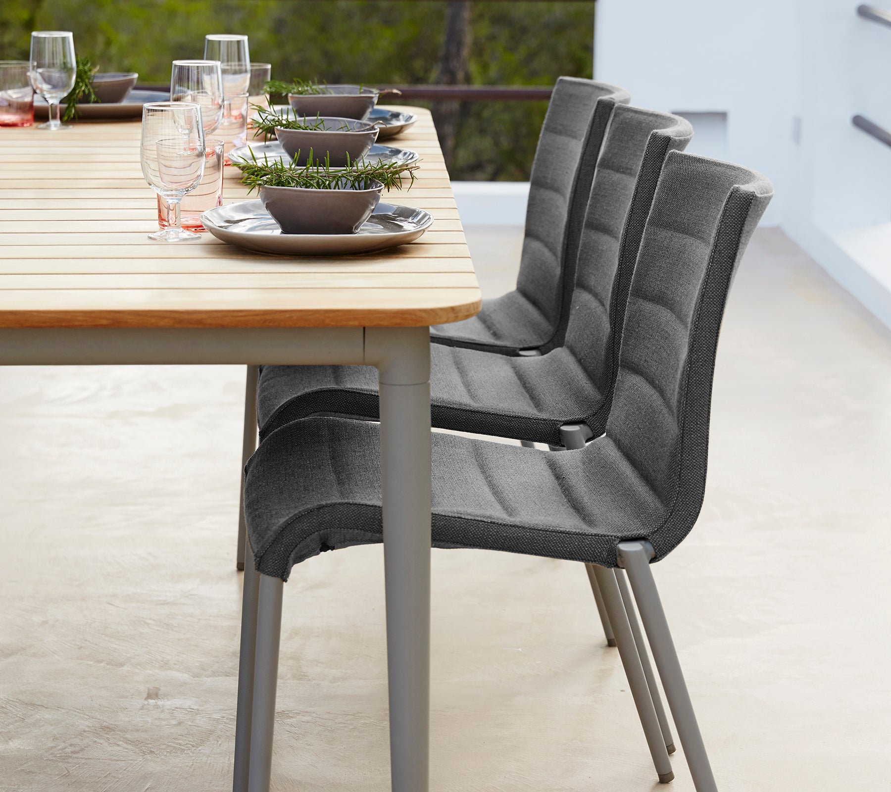 A modern dining setup featuring a wooden table with plates, glasses, and three stylish gray chairs arranged neatly.