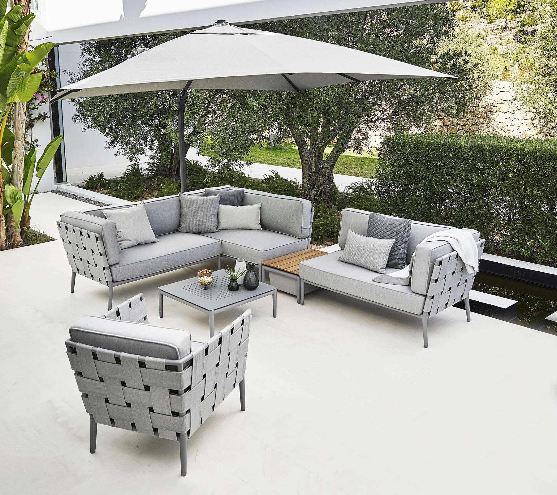 Stylish outdoor seating arrangement featuring a grey sectional sofa, armchair, and coffee table under a large umbrella.
