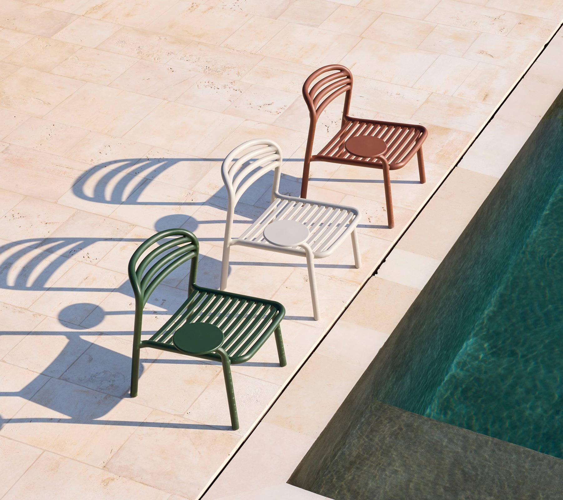 Three modern chairs in green, white, and brown beside a swimming pool.
