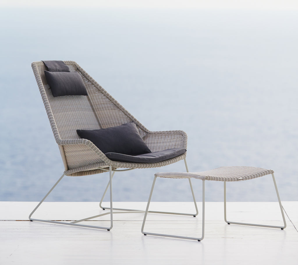 Modern grey chair with black cushion and grey ottoman by a scenic backdrop.