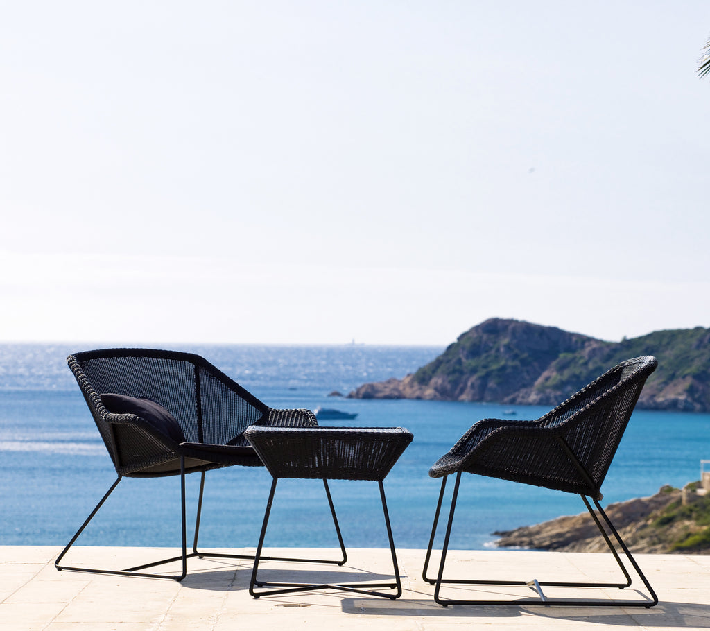 Two black chairs and a black table with a coastal view.