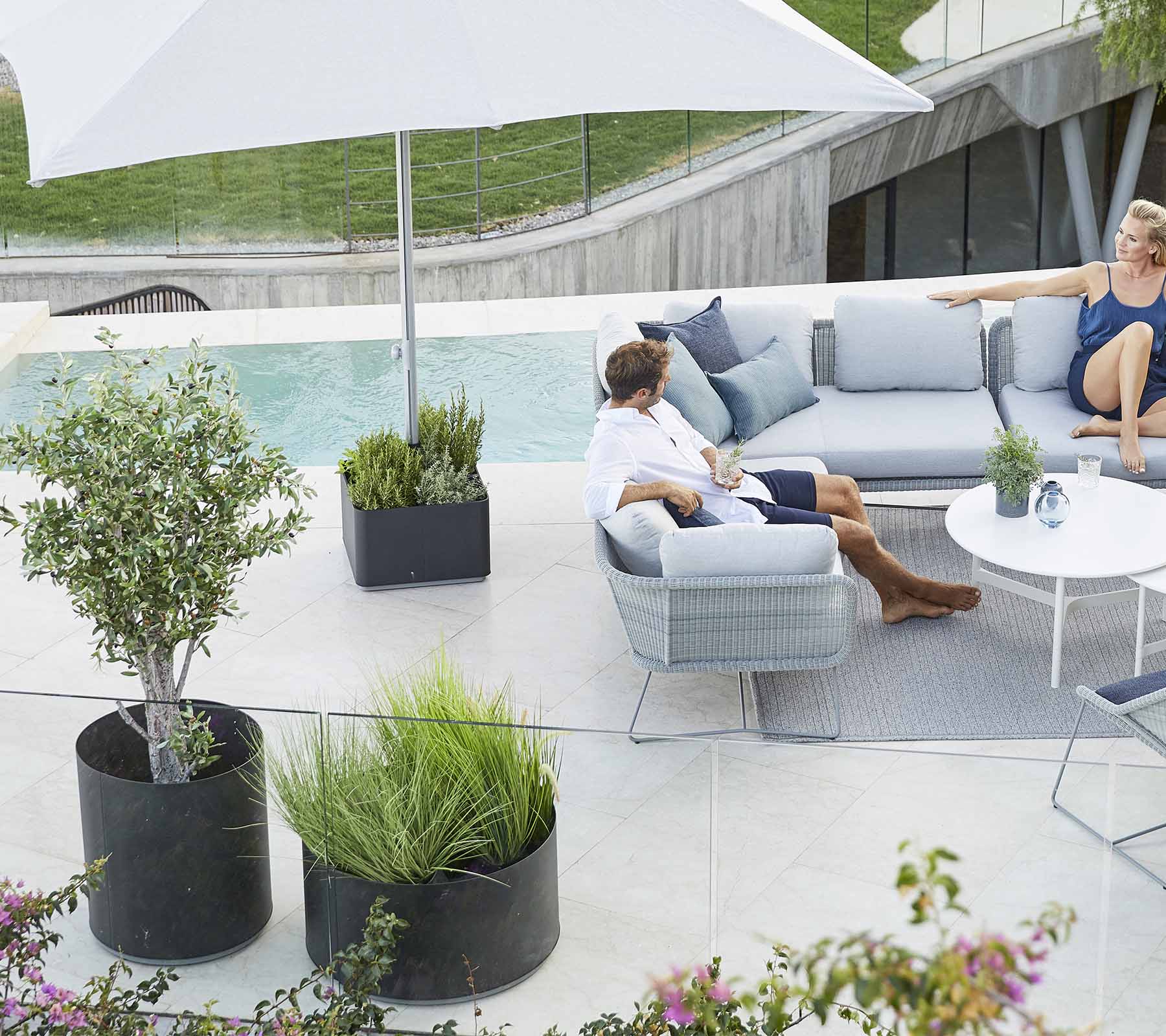 A stylish outdoor seating area featuring a comfortable sofa, plants, and a large umbrella, perfect for relaxation.