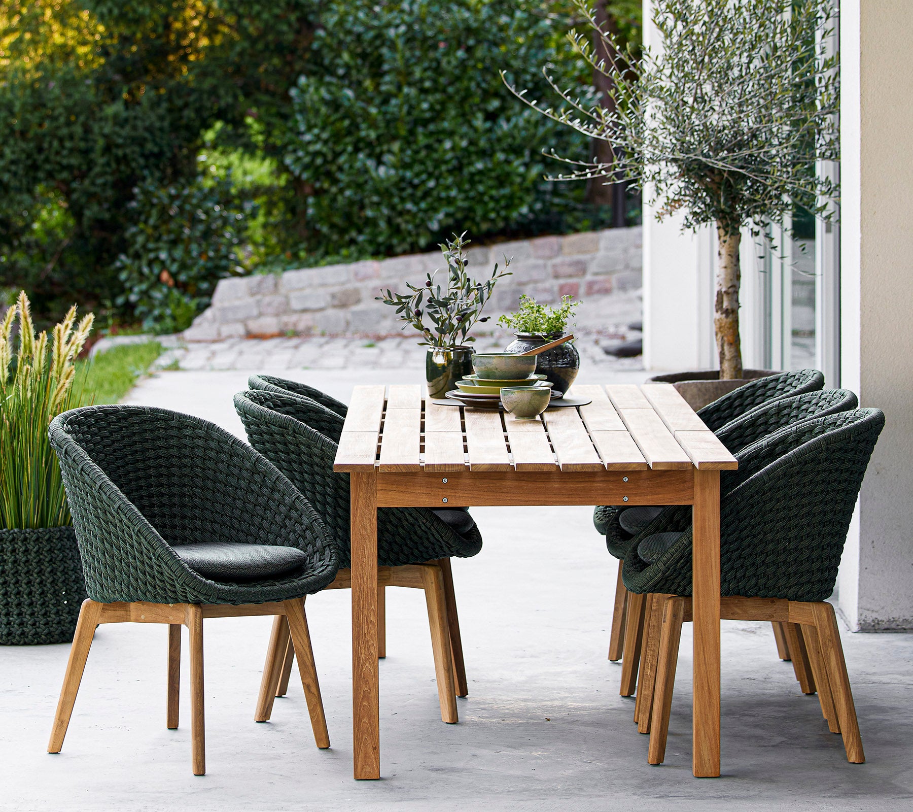 A wooden table surrounded by stylish green chairs, with decorative plants and a serene background. Ideal for dining or relaxation.