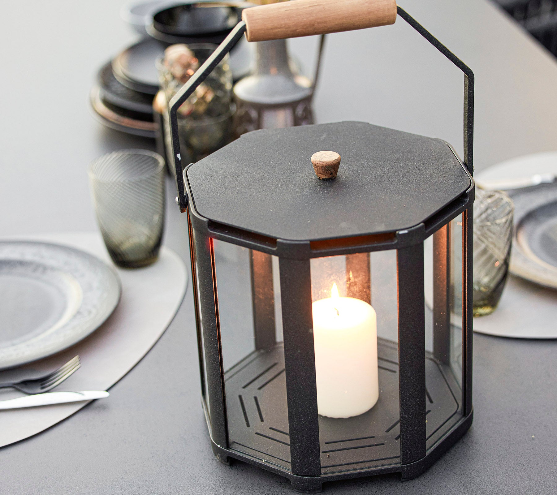 A stylish octagonal lantern featuring a central candle, surrounded by glass panels and a wooden handle, enhancing any setting.