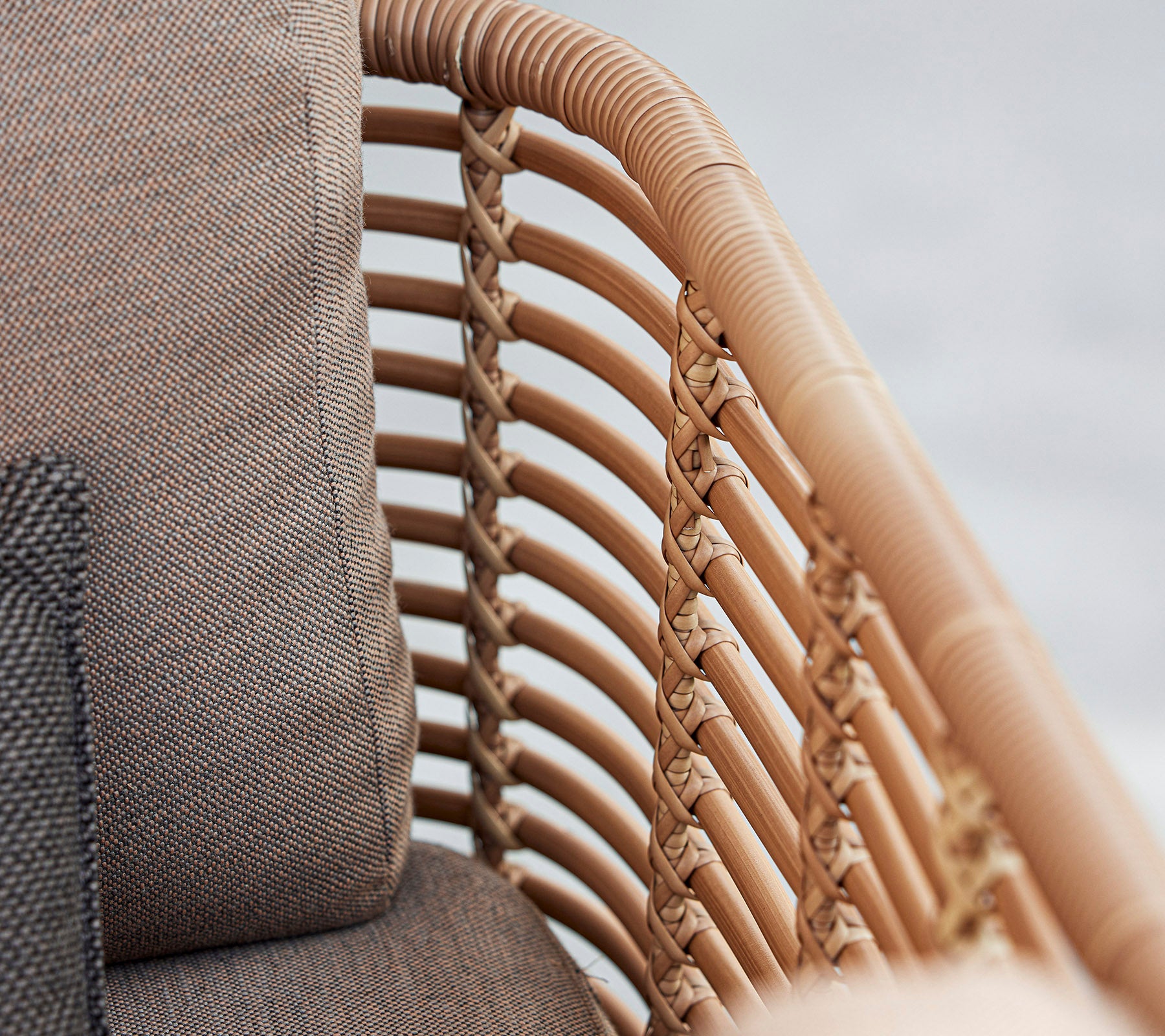 Close-up of a stylish armchair featuring woven rattan details and soft cushions in neutral tones, showcasing modern design.