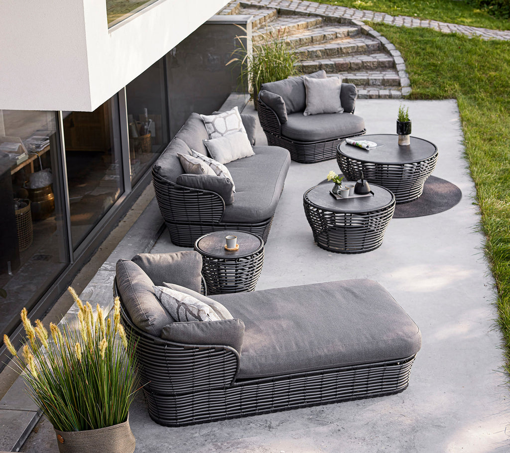 Stylish outdoor seating arrangement featuring a gray sectional, armchairs, and tables, complemented by decorative pillows and plants.